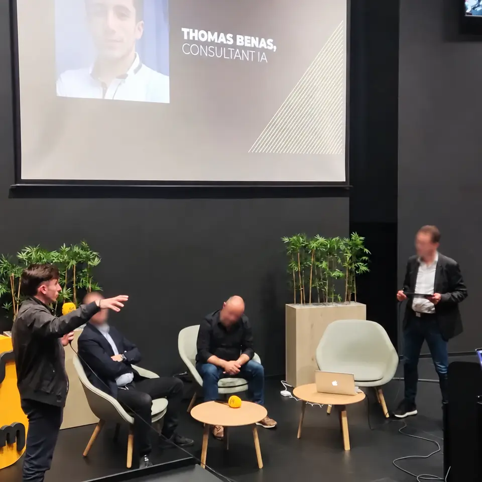 Thomas sur scène, micro en main, lors d'une table ronde ; l'écran affiche « Thomas BÉNAS, consultant IA ».